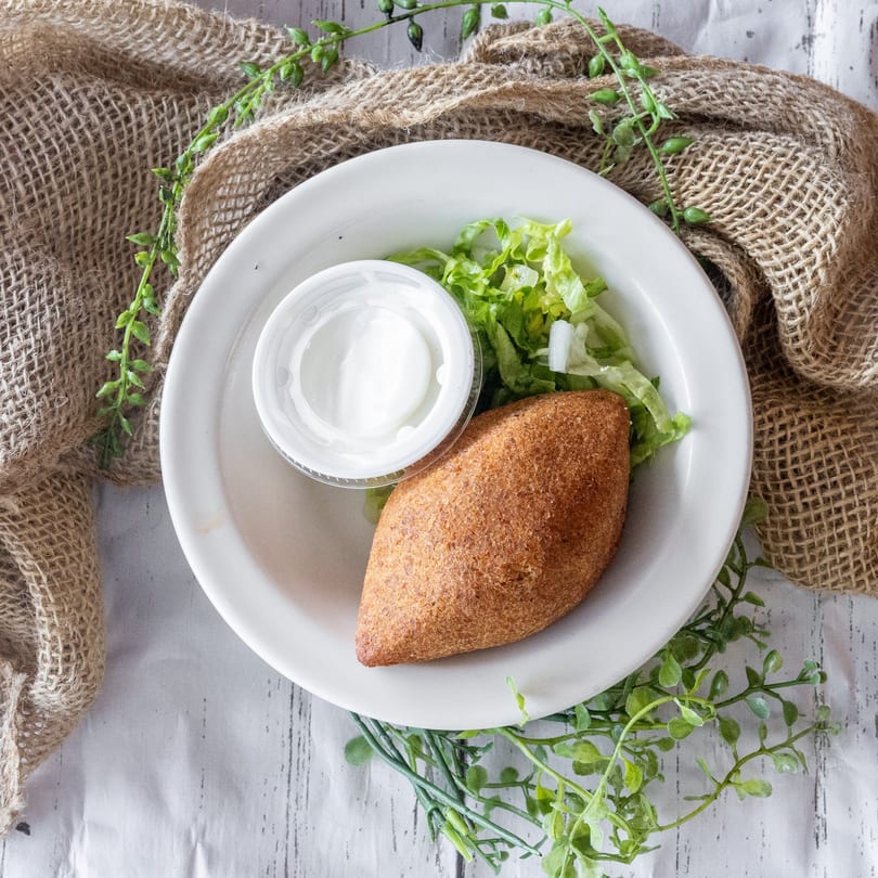 Fried kibbeh on a white plate with a side of lettuce and a container of white sauce.