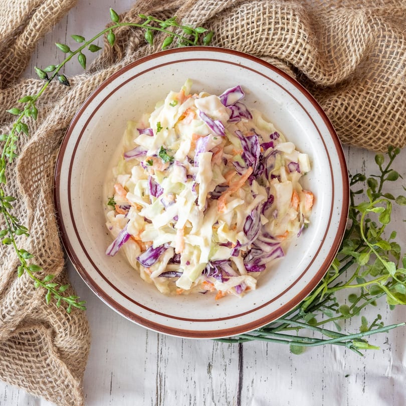 Creamy coleslaw with shredded green cabbage, red cabbage, and carrots in a white bowl.