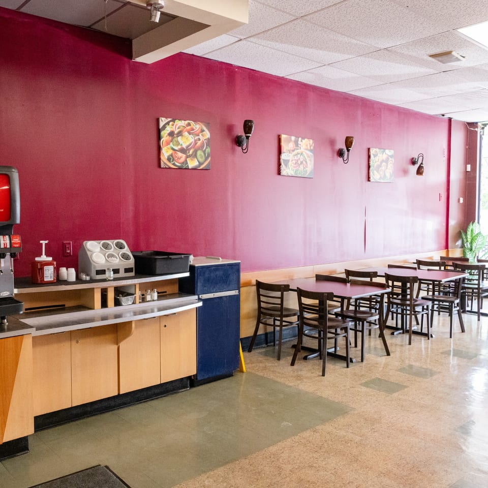 Empty restaurant interior with red walls, dark tables and chairs, and a self-serve drink station.