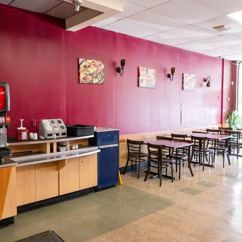 Empty restaurant interior with red walls, dark tables and chairs, and a self-serve drink station.