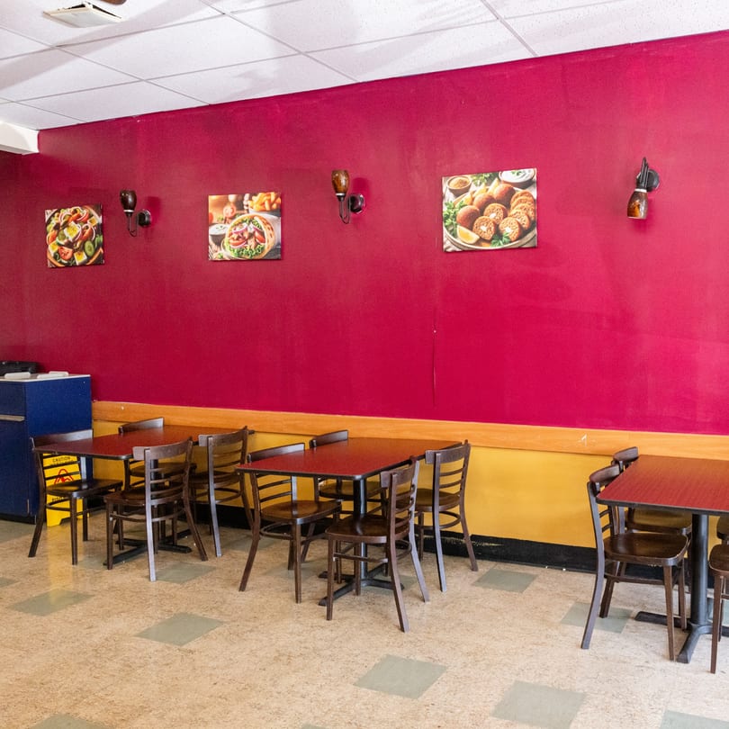 Empty restaurant dining area with red and yellow walls, brown tables, and food pictures.