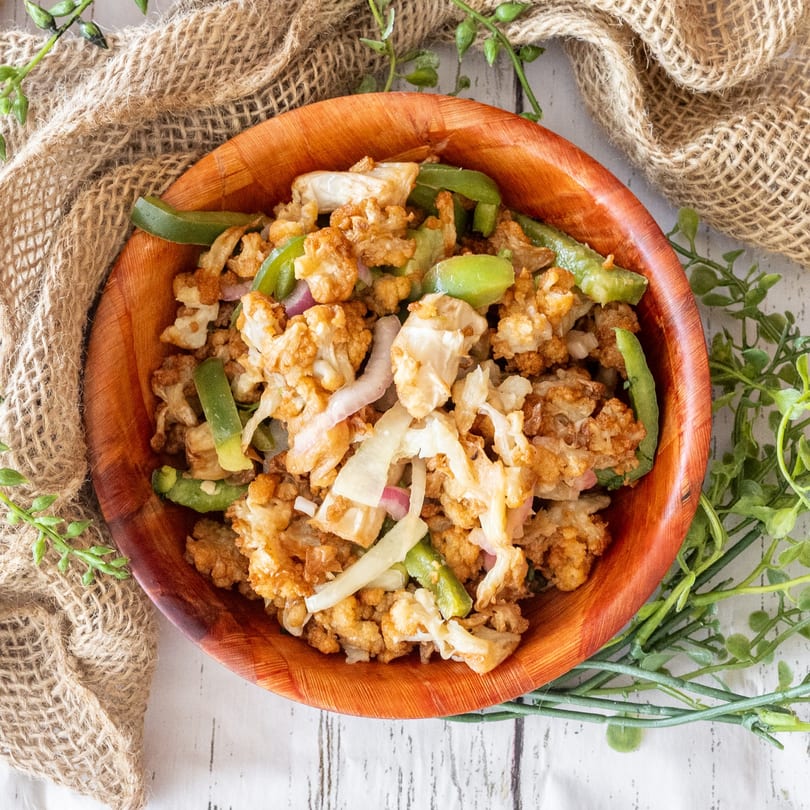 Top-down view of a wooden bowl filled with fried cauliflower, green peppers, and onions.