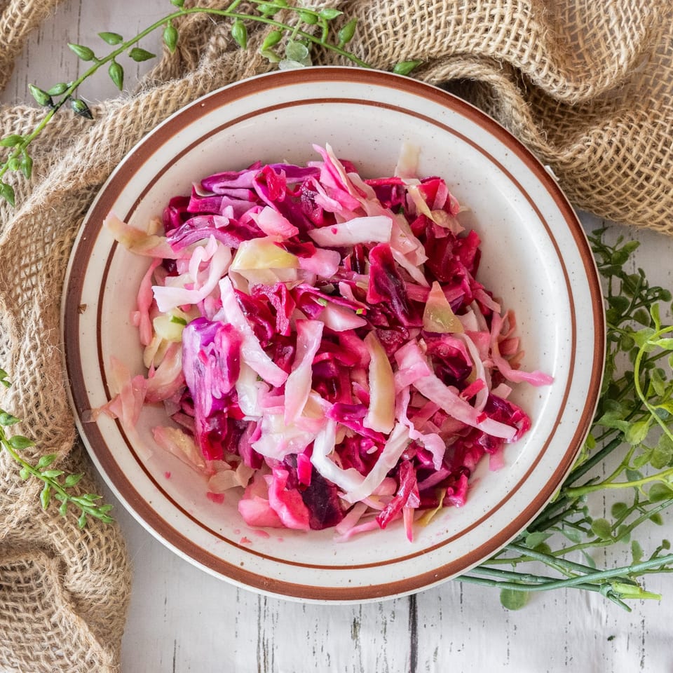 A bowl of vibrant pink and purple shredded cabbage salad on a white wooden table.