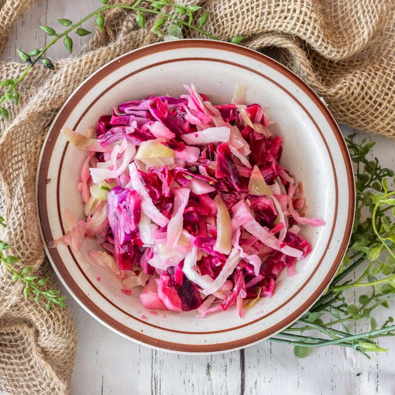 A bowl of vibrant pink and purple shredded cabbage salad on a white wooden table.