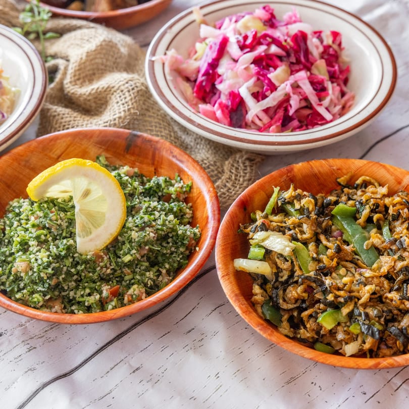 Three bowls of Middle Eastern food, including tabbouleh, pickled cabbage, and a stir-fry dish.