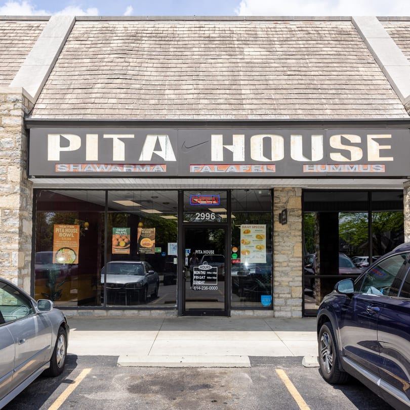 The exterior of Pita House restaurant, featuring a stone facade, large windows, and a prominent sign.