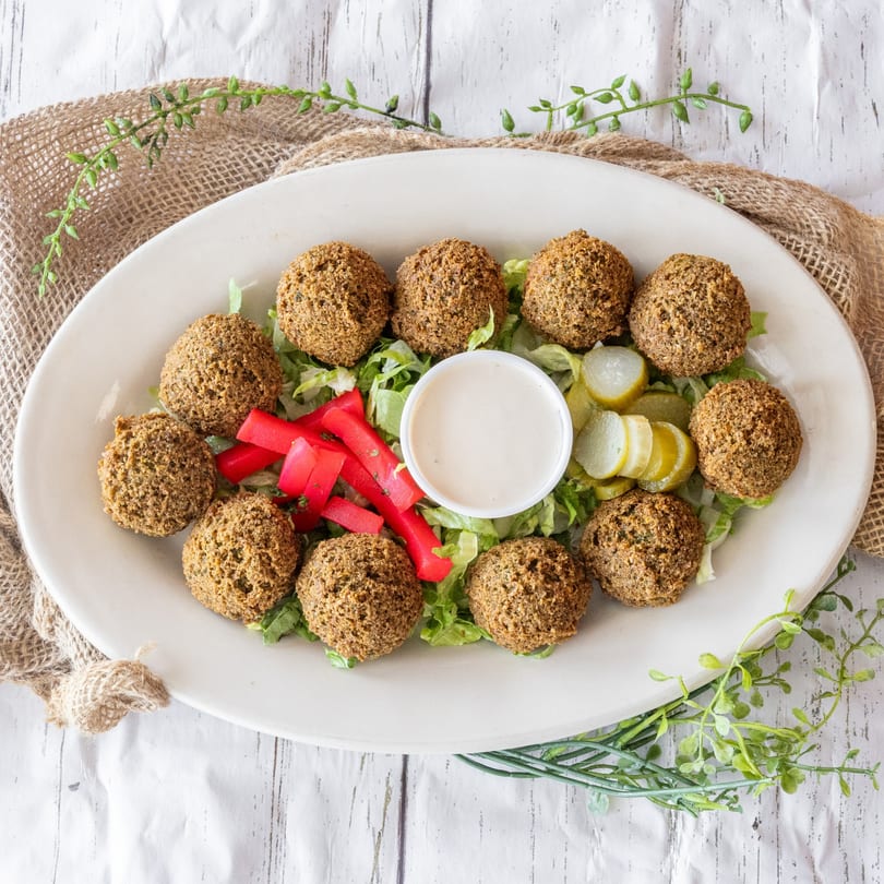A platter of falafel balls on lettuce with pickled vegetables and a white dipping sauce.