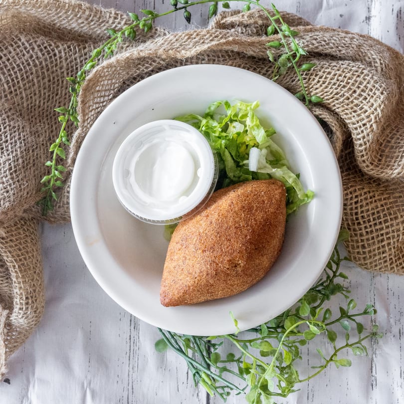 Fried kibbeh on a white plate with shredded lettuce and a side of white sauce.