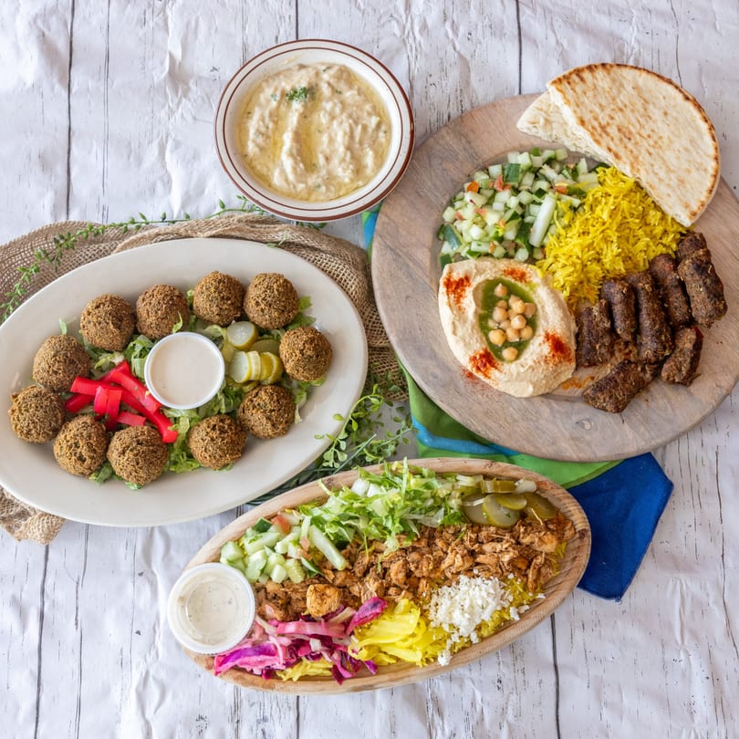 A top-down view of three Middle Eastern platters with falafel, hummus, rice, and meat.
