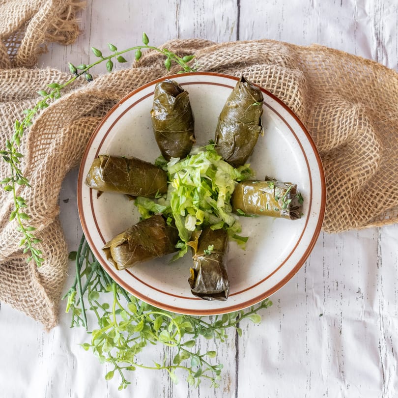 Six dolmades, or stuffed grape leaves, arranged around a small pile of shredded lettuce on a plate.