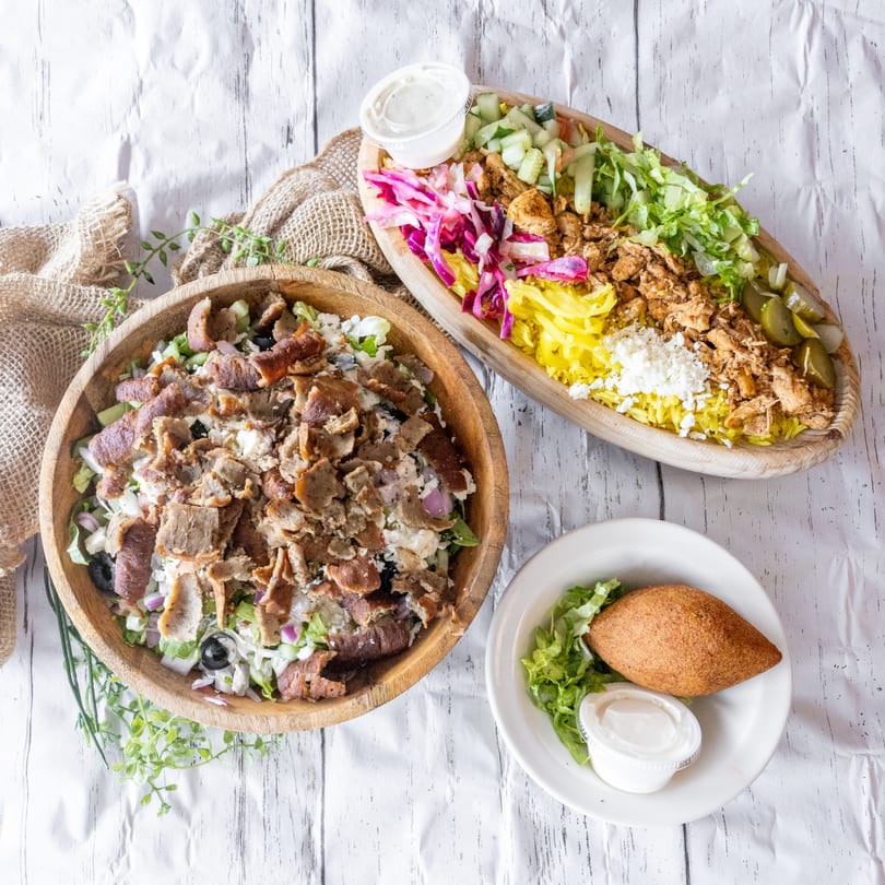 Two large bowls of Mediterranean food, one with gyro meat and salad, the other with chicken and rice.