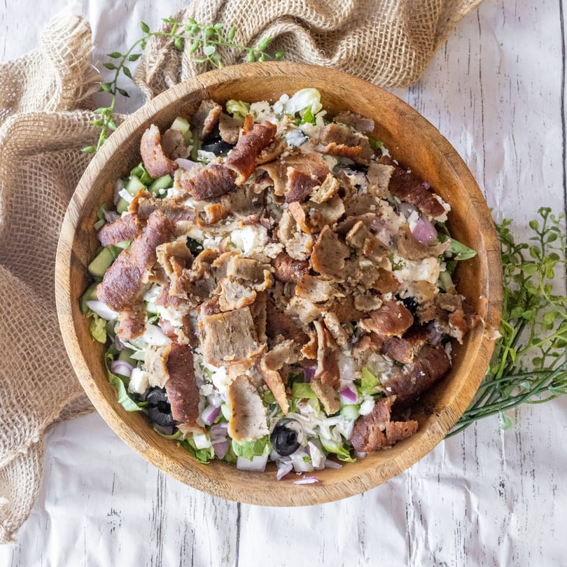 Overhead view of a wooden bowl filled with a gyro salad on a white and burlap background.