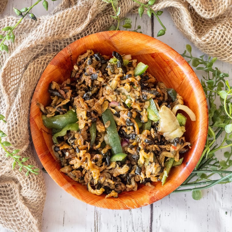 A wooden bowl filled with a stir-fry of black and brown ingredients, green peppers, and onions.